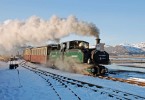 Steam train pulling carriages through a snowy landscape